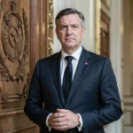 Homme politique français en costume sombre devant une porte institutionnelle ornée, symbolisant les pouvoirs exceptionnels de l'article 16 de la Constitution